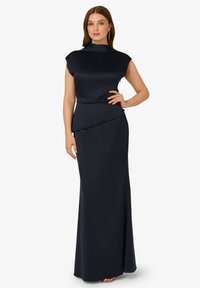 Námořnická modrá saténová večerní róba s vysokým límcem, rukávy ve tvaru kapes a drapovaným detailem v pase, splývá do rovné sukně až na zem.