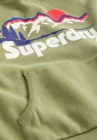 Olivově zelená mikina s kapucí se grafikou hory v červené a modré barvě, s logem "Superdry" v tučné bílé. Měkký materiál s přední kapsou.