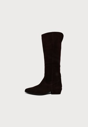 Une botte marron foncé montant jusqu’au genou, avec un bout pointu, un talon carré bas et une couture latérale, sur un fond clair uni.