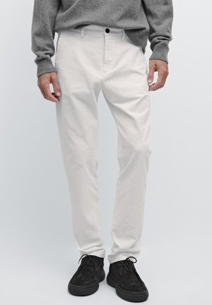 Pantalon en coton blanc à coupe ajustée, avec poches latérales et fermeture à boutons, associé à des chaussures en daim noir à lacets.