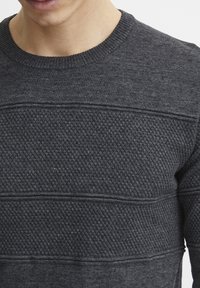 Pulover gri închis din cărbune, cu un model texturat de tricot, guler rotund cu margini ribburate și detalii cu dungi orizontale. Material moale și cald.