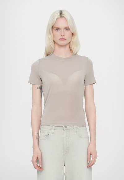 T-shirt beige aderente con maniche corte, scollatura rotonda e leggero effetto vedo-non vedo nella parte anteriore. Indossato con jeans chiari e morbidi.
