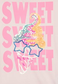 Šviesaus atspalvio marškinėliai, dekoruoti spalvingu, blizgančiu ledų kūgio dizainu su rožinėmis, geltonomis ir mėlynomis detalėmis bei dideliu užrašu "SWEET".
