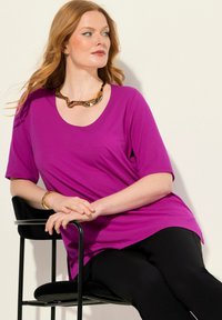 Top viola a maniche corte con scollatura a barco, realizzato in tessuto morbido, abbinato a leggings neri e accessoriato con una collana d'oro.