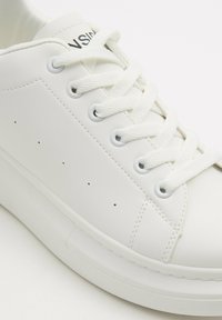 Zapatilla blanca con parte superior sintética lisa, puntera redonda y cordones planos. Cuenta con ojales metálicos y perforaciones mínimas para la transpirabilidad.