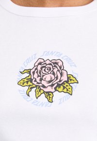 Hvit ribbet t-skjorte med et sentralt grafisk motiv av en rosa rose med grønne blader, omgitt av blå tekst som leser "SANTA CRUZ."