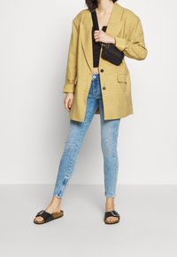 Żółta, w kratkę, oversize'owa marynarka, czarny crop top, jasnoniebieskie dopasowane dżinsy oraz czarne klapki z detalem w postaci klamry.