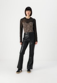 Pantaloni neri in pelle a vita alta abbinati a un body con stampa leopardata, dotato di maniche lunghe trasparenti nere. Gli accessori includono una piccola borsa a spalla.