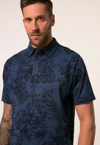 Kortärmad pikétröja i mörk marinblå färg med ett subtilt mönster av blommor och blad, knäppt krage och mjukt, strukturerat tyg.