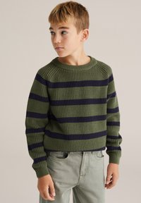 Zaļš adīts džemperis ar tumši ziliem svītrām, apaļu izgriezumu un ribinātām aprocēm. Nēsāts ar gaiši zaļām biksēm, kas uzrāda brīvu piegriezumu.