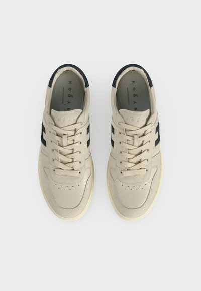 Paire de baskets en cuir beige avec des accents latéraux noirs et des lacets, vues de dessus sur fond blanc.