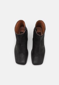 Botas de tobillo de cuero negro con una textura suave, punta cuadrada y cremalleras laterales. Las plantillas marrones complementan el diseño. Silueta estrecha.