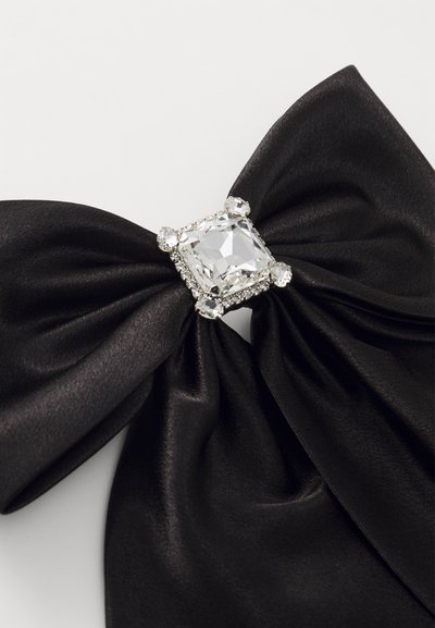 Svart satin sløyfe med en stor rektangulær klar edelsten i midten, omkranset av mindre steiner, med en jevn tekstur og elegant design.