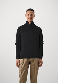 Schwarzer Pullover mit Reißverschluss am Hals, mit gerippter Textur und langen Ärmeln. Leichter Stoff mit einer figurschmeichelnden Passform und kontrastierenden Nähdetails.