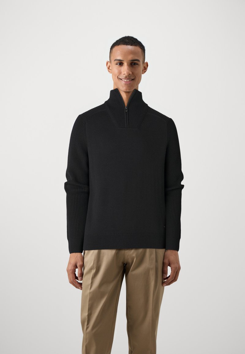 Schwarzer Pullover mit Reißverschluss am Hals, mit gerippter Textur und langen Ärmeln. Leichter Stoff mit einer figurschmeichelnden Passform und kontrastierenden Nähdetails.