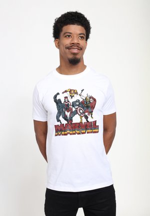 Man draagt een wit T-shirt met daarop Marvel-superhelden Black Panther, Scarlet Witch, Captain America, Thor en Iron Man boven het rode Marvel-logo.
