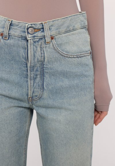 Hellblaue Jeans aus Denim mit hoher Taille, fünf Taschen und kontrastierenden orangen Nähten. Mit einem Metallknopfverschluss und klassischer Passform.