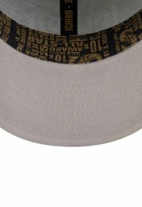 Helle graue Baseballmütze mit einer schwarzen und goldenen bedruckten Schweißbandunterseite, die Text und Sterngrafiken zeigt.