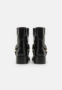 Botas de tobillo de cuero negro con textura de cocodrilo, detalles en hardware dorado y un tacón robusto. Presenta dos hebillas laterales y una suela resistente.
