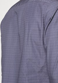 Donkerblauwe shirt met een geometrisch patroon; textiel met een gestructureerde stof en een gladde afwerking bij de kraag, en een licht gestructureerde silhoutte.