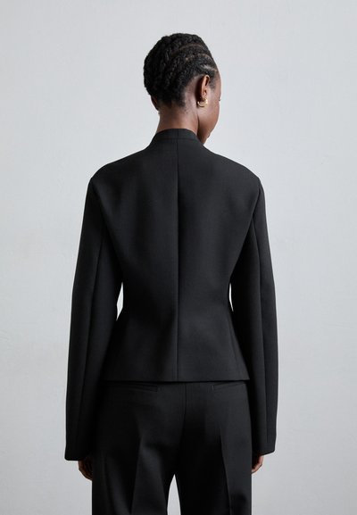 Μαύρο σακάκι κομμένο, χωρίς γιακά, με δομημένους ώμους και μακριά μανίκια. Διαθέτει κομψό, μινιμαλιστικό σχέδιο και κομψή σιλουέτα.