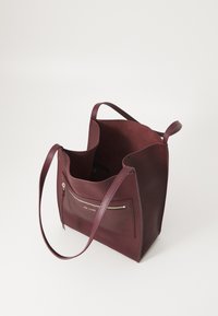 Bordeaux læder tote taske med en tekstureret finish, åben top, to skulderremme og en frontlomme med lynlås. Indvendig har den en suede-agtig overflade.