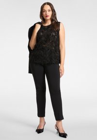 Top nero senza maniche con design a frange testurizzate, abbinato a pantaloni neri slim e scarpe nere con tacco alto caratterizzate da dettagli a fiocco.