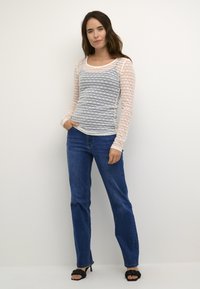 Lichte langekooltop met een blauw gestreept patroon op een crèmekleurige basis, gecombineerd met donkerblauwe rechte jeans en zwarte hoge hakken sandalen.