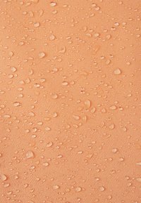 Gouttelettes d'eau de différentes tailles dispersées sur un tissu ou une surface imperméable lisse de couleur pêche.