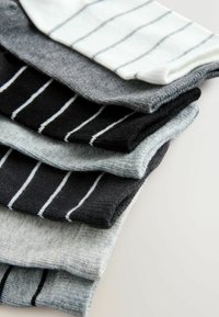 Pile de chaussettes rayées pliées en noir, blanc, gris et bleu clair sur une surface claire.
