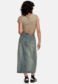 Lyseblå denim maxiskjørt med høy livhøyde, to baklommer, og synlig søm. Sammen med en beige croppet topp og svarte joggesko.
