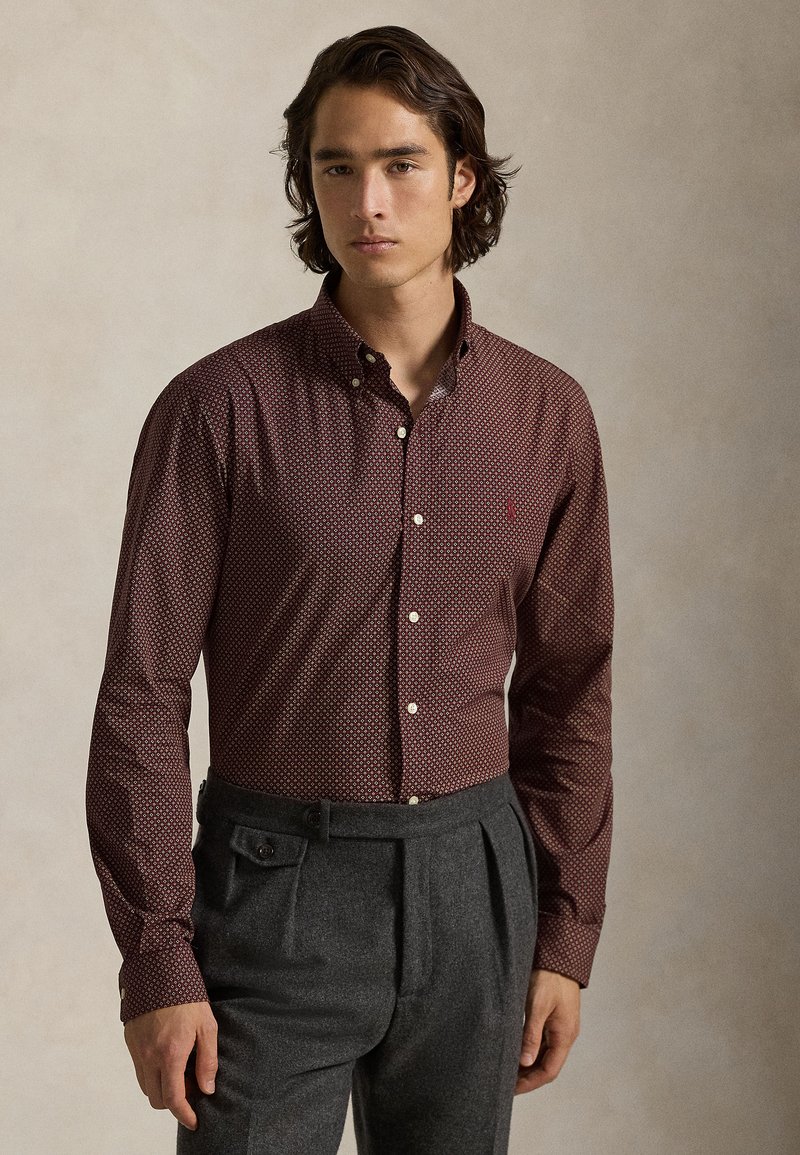 Camisa de botão de manga longa com padrão vermelho, colarinho e botões brancos. Combinada com calças cinzentas de cintura alta com bolsos laterais.