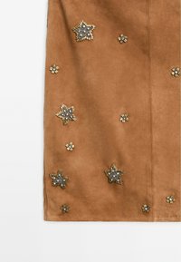 Braunes Wildleder mit Stern- und Blumenverzierungen in Gold- und Silbertönen. Hat eine glatte Textur und dekorative Nähte.
