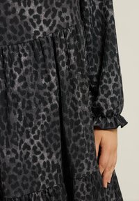 Sukienka w czarno-szary wzór w panterę, z falbaniastymi rękawami, warstwową strukturą i teksturowanym materiałem. Zbliżenie na detale tkaniny.