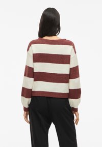 Sweater com largas riscas em bordeaux e creme, feito de um material de malha suave. Apresenta um corte relaxado, ombros caídos e punhos canelados.