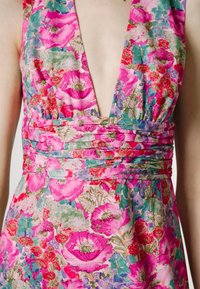 Robe fleurie avec un décolleté en V, un corsage plissé et des motifs vibrants rose, vert et violet sur un tissu léger.