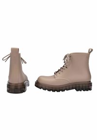 Botas de tobillo de goma beige con punta redonda, parte delantera con cordones y suela gruesa y transparente; cuenta con un lazo en la parte posterior y marca grabada.