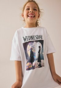 Vit bomull t-shirt med en färgglad grafisk tryck av två karaktärer mot en bakgrund av färgat glas. Rund hals och korta ärmar.