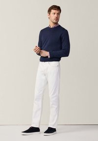 Maglione navy, jeans bianchi e sneakers nere. Il maglione ha un colletto rotondo; i jeans sono slim fit con tasche frontali.