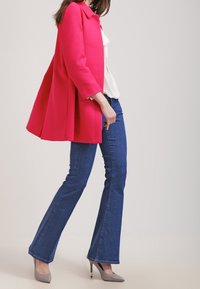 Fuksianvärinen räätälöity takki, jossa on jämäkkä muotoilu, yhdistettynä sinisiin leveälahkeisiin farkkuihin ja harmaisiin kärkitossuihin. Siistit linjat, teksturoitu kangas.