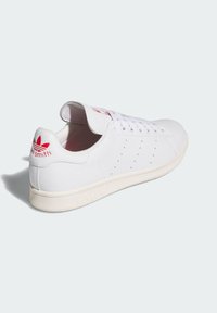 Vita lädersneaker med perforerade detaljer, med en röd logotyp på tungan och hälen, samt en krämfärgad gummisula.
