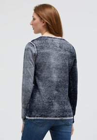 Langärmliges Oberteil mit einem verlaufenden blau-grauen Muster, runder Ausschnitt, kontrastierenden Nähten und entspannter Passform. Kombiniert mit Jeans.