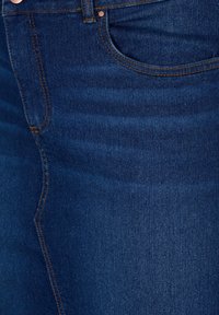 Temno modri jeans iz denima z gladko teksturo, kontrastnim oranžnim šivom, sprednjim žepom in zadrgo ter gumbom za zapiranje.