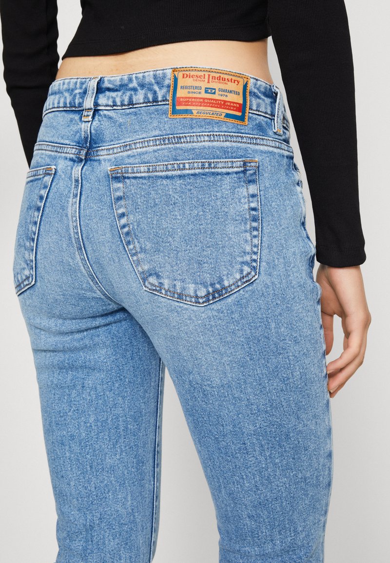 Verblasste hellblaue Jeans mit hintenliegenden Taschen, einem Markenpatch auf der Rückseite und einem schmalen Schnitt mit sichtbaren Nähten.