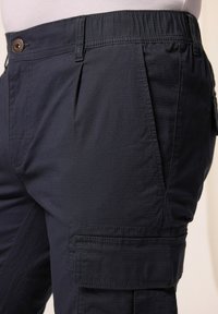 Námořnické cargo kalhoty s texturovanou tkaninou, elastickým pasem, předními záhyby a boční kapsou na našití. Mají zapínání na knoflík.