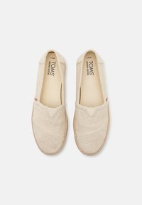 Beige Leinenschuhe zum Hineinschlüpfen mit strukturiertem Obermaterial, elastischen Seitenbündchen und einer hellbraunen Gummisohle. Logo auf der Innensohle gedruckt.
