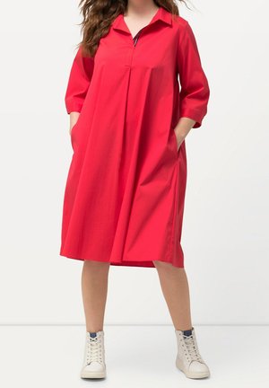 Robe rouge, longueur genou, avec un col, des manches courtes, des poches latérales et une coupe décontractée. Le tissu semble lisse avec une texture subtile.
