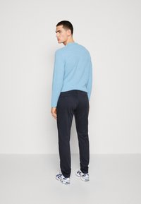 Maglione azzurro chiaro con texture, pantaloni neri con tasche posteriori e sneakers bianche con dettagli blu. Modello mostrato di spalle.