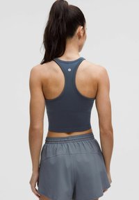 Sivi sportski crop top s dizajnom na leđima, uparen s odgovarajućim sivim šortsem s elastičnom strukom i glatkom teksturom.