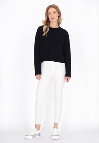 Maglione cropped a trecce navy abbinato a jeans skinny bianchi e sneakers platform bianche. Semplice scollatura rotonda, maniche lunghe.